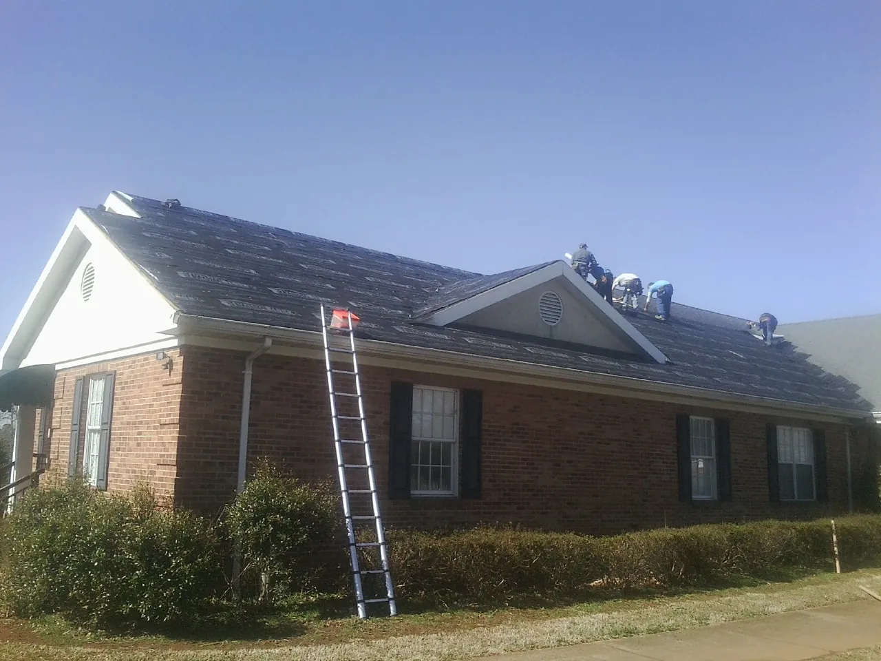 Crew tearing shingles off a brick ranch roof with a ladder set — Metal Roof Repair work by our crew in Gretna